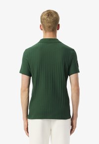 Grön ribbat polo med krage, korta ärmar och en logotyp på vänster axel. Slät textur, figursydd design.