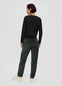 Czarna długa koszula z długim rękawem w połączeniu z ciemnozielonymi spodniami z korduroju, charakteryzującymi się prostym krojem i subtelnymi pionowymi paskami, noszona z jasnymi butami.