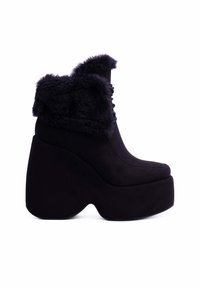 Stivali alla caviglia neri con plateau e punta rotonda, dotati di un bordo in pelliccia sintetica e un design della chiave a forma sculpturale e chunky. Materiale morbido simile al camoscio.