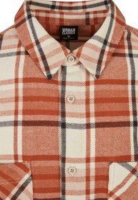 Plaid shirt in orange, cream, and black tones. Made of textured fabric, featuring a buttoned collar and chest pocket detail. Urban Classics label.