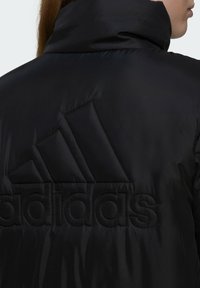 Zwarte gewatteerde jas met een hoge kraag, textuurstof en groot reliëf Adidas-logo op de rug, met geometrische logoaccenten.