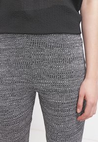 Leggings gris à motifs en tissu texturé, présentant un design géométrique avec des nuances variées de gris clair et foncé.