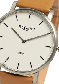 Montre ronde à cadran blanc avec un boîtier en acier inoxydable, des marqueurs d'heure noirs et un bracelet en cuir tan. Présente les marques REGENT et TITAN.