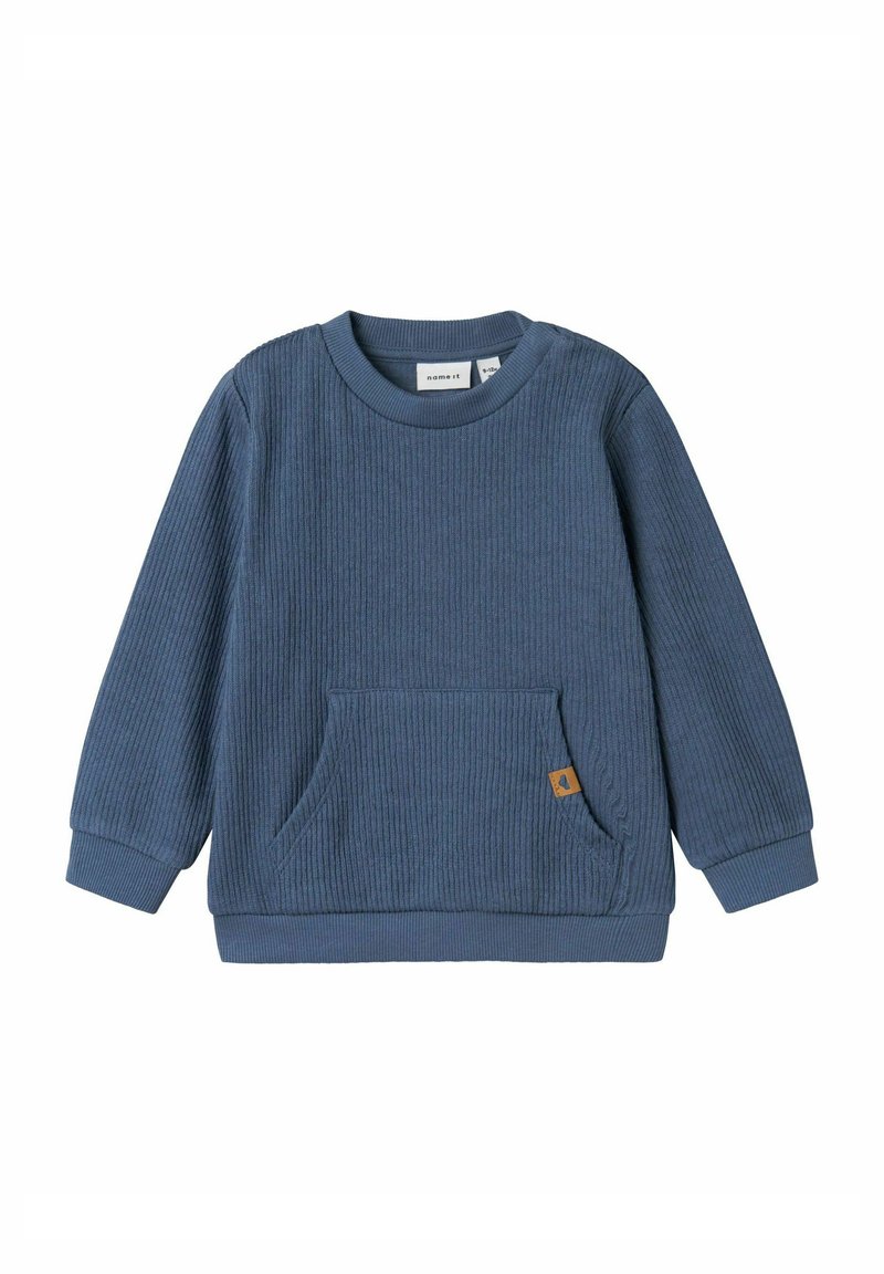 Felpa blu a costine con maniche lunghe, scollo rotondo e una tasca frontale. Presenta un piccolo etichetta marrone sulla tasca. Tessuto morbido.