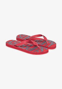 Tongs rouges avec le texte gris "Superdry" sur la semelle, dotées de fines lanières et de semelles texturées pour une meilleure adhérence.