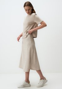Haut en tricot beige clair et jupe assortie, avec une coupe décontractée, une texture douce et une silhouette évasée. Porté avec des baskets blanches.