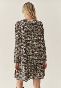 Juoda suknelė su rusvu abstrakčiu raštu, ilgomis rankovėmis, susikaupusiu liemeniu ir klostuota sijonu. Medžiaga turi lygų paviršių.