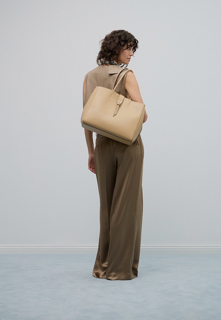 Beige Lederhandtasche mit einer strukturierten Form und langen Tragriemen. Die Tasche verfügt über ein minimalistisches Design und eine flache, glatte Textur.