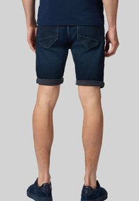 Ciemne dżinsowe szorty z podwiniętymi mankietami, z tylnymi kieszeniami z delikatnym detalem w postaci szwu. Włożone z granatowymi trampkami, prezentujące casualowy styl.