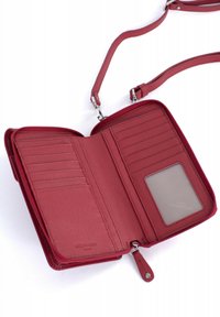 Portafoglio in pelle rossa con chiusura a zip, scomparti per carte interne, finestra trasparente per l'ID e tracolla rimovibile; superficie testurizzata.