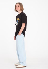 Camiseta gráfica negra con un diseño colorido, combinada con jeans de pierna ancha de color azul claro y zapatillas blancas con suelas marrones.