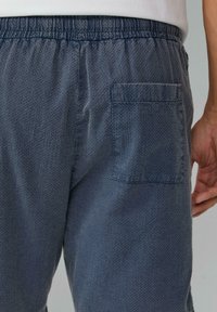 Dunkelblaue, strukturierte Jogginghosen mit einem elastischen Bund und einer einzelnen Gesäßtasche. Der Stoff hat ein dezentes, erhabenes Muster.