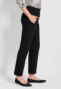 Zwarte broek met een tapering fit, met een platte tailleband, zakken en opgerolde manchetten. Gecombineerd met zwarte flats met net-accenten.
