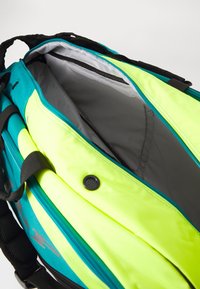 Rucksack mit leuchtend gelben und türkisfarbenen Paneelen, Reißverschluss, geräumigem Innenraum mit grauer Fütterung und schwarzen verstellbaren Trägern.