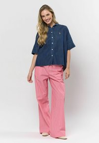 Džínsová košeľa na gombíky s krátkymi rukávmi a nášivkou na hrudi, v kombinácii s bledoružovými pruhovanými širokými nohavicami. Textúrovaná látka, voľný strih.