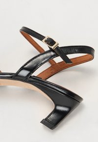 Sorte strappy sandaler med en blank lærfinish, som har en liten blokkheel og et gullspenne på ankelremmen.