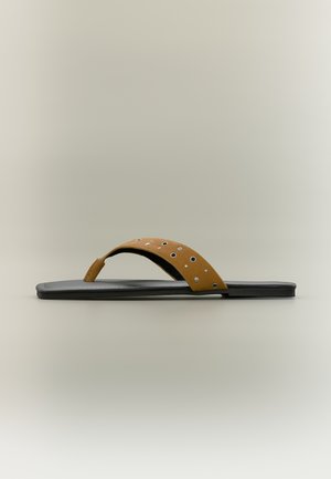 Zwarte platte sandaal met een bruine leren teenband voorzien van zilveren studs en metalen oogjes tegen een effen achtergrond.