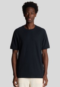 T-shirt in cotone nero con maniche corte, colletto rotondo e vestibilità rilassata. Tessuto morbido, cuciture minime e senza motivi o dettagli visibili.