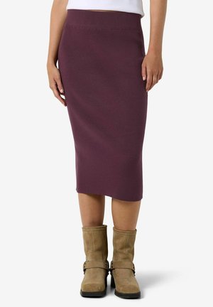 Jupe côtelée violette longueur genou portée avec des bottines en suède couleur camel et un top blanc, présentée sur une personne debout sur fond uni.