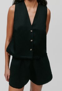Czarny top bez rękawów z dekoltem w kształcie litery V, z dwoma guzikami z przodu, frędzelkowym dołem i luźnym krojem, zestawiony z dopasowanymi czarnymi szortami.