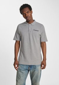 Szara koszulka polo z bawełny, z kołnierzykiem, krótkimi rękawami i subtelnym logo na lewej piersi. Połączona z niebieskimi jeansami.