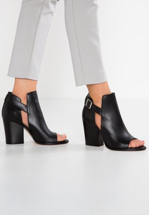 Sorte åbne hæl ankelsko lavet af glat læder. Har udskåret design, lille spænde og en chunky hæl.