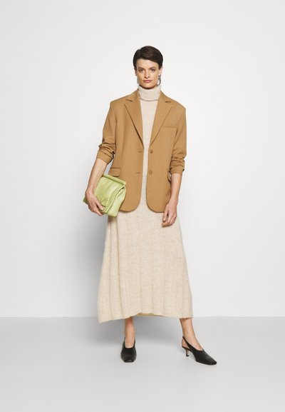 Blazer castanho ajustado, vestido creme em texturas caneladas, saltos pretos tipo slingback, e uma mala de mão verde clara. Estilo minimalista, texturas suaves.