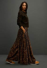 Long leopard-print skirt with dark brown cropped cardigan, featuring buttons. Black and mustard sneakers complete the look, set against a grey background.