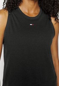 Top senza maniche nero realizzato in tessuto morbido, con un piccolo logo rosso, bianco e blu sul petto e scollatura rotonda.