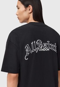 Sort t-shirt med korte ærmer og løs pasform, med hvidt broderet tekst "AllSaints LONDON" på ryggen. Bomuldsmateriale.