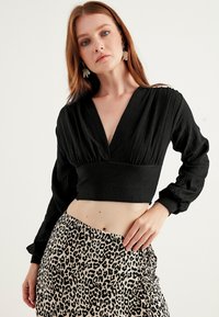 Blusa nera cropped con tessuto testurizzato e scollatura a V profonda. Abbinata a una gonna a fantasia leopardata con dettagli arricciati e spacco alto.