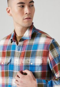 Heren flanellen shirt met een meerkleurig ruitpatroon in rood, blauw, groen en wit, voorzien van knoopzakken op de borst en een kraag.