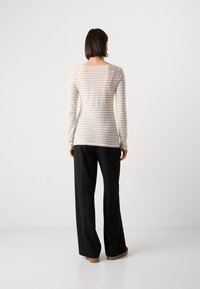 Stripete langermet skjorte i lys krem og beige, mykt stoff, avslappet passform, paret med svarte vide bukser og brune slip-on sko.