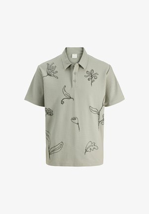 lichtgroene, geribbelde polo met geborduurde botanische ontwerpen in donkergroen. Heeft een kraag en drie knopen bij de halslijn.