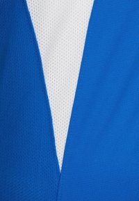 Sininen ja valkoinen urheilupaita, jossa on verkkokuviointi, V-pääntie ja kontrastiväriset paneelit. Kevyt kangas.