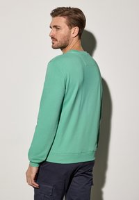 Mintgrön sweatshirt med rund hals, långa ärmar och ribbade manschetter. Har en enkel design och tygtextur, bärs över marinblå cargobyxor.