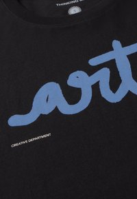 T-shirt noir avec un grand lettrage manuscrit bleu "art" et un petit texte blanc "CREATIVE DEPARTMENT" sous le motif, près du col.