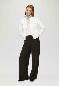 Witte denim jack over een crème top, gecombineerd met zwarte wijde broek. Accessoires zijn een gestreepte sjaal en zwarte schoenen.