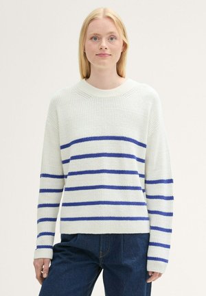 Weißer Strickpullover mit blauen horizontalen Streifen. Runder Halsausschnitt, lange Ärmel, lockere Passform. Getragen mit dunkelblauen Jeans. Strukturierter Stoff.