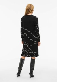 Abito in maglia nera con motivi a linee bianche. Maniche lunghe, collo rotondo, lunghezza al ginocchio, abbinato a stivali neri alti fino al ginocchio. Texture liscia.