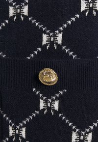 Pull en maille marine avec des motifs de nœuds blancs. Présente un bouton décoratif en or centré à la taille avec une finition texturée.