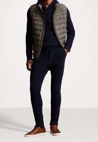 Marinblå stickad träningsdräkt med huva, kombinerad med en grå vadderad väst och bruna lädersneakers. Har en ribbad textur och dragsko i midjan.