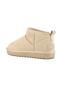 Botas de tobillo de ante beige con punta redondeada, costuras mínimas y suela texturizada. Cuenta con una pequeña lengüeta en el talón para facilitar su uso.