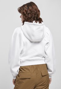 Felpa corta bianca con cappuccio, dotata di maniche voluminose e orlo a coste. Abbinata a pantaloni cargo marrone chiaro con tasche posteriori.