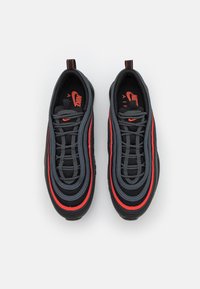 Nike Air Max 97 sneakers featuring a black mesh and rubber upper with red and grey wave patterns, textured laces, and a prominent logo.