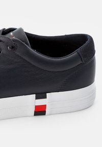 Baskets en cuir bleu marine avec un dessus texturé, lacets noirs et une semelle en caoutchouc blanche avec des accents de rayures rouges et noires.