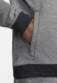 Gray athletic sweatshirt featuring a textured fabric, black ribbed cuffs, and a side pocket on the left side.