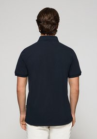 Camiseta polo azul marino de manga corta, con collar clásico, puños de tejido plano y dobladillo recto. Diseño minimalista sin patrones ni adornos visibles.