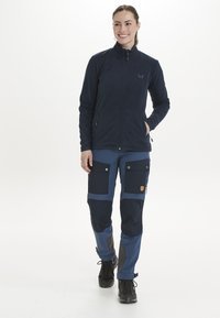 Veste en polaire marine avec un col haut, associée à un pantalon marine et bleu foncé avec des poches. Tissu durable avec des accents de genoux renforcés.