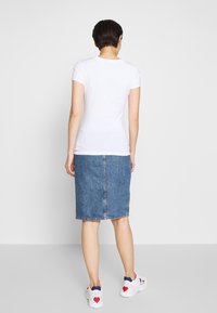 Bílá tričko s krátkým rukávem kombinované s modrou denimovou tužkovou sukní. Obuv má kombinaci bílé barvy s červenými a modrými akcenty.